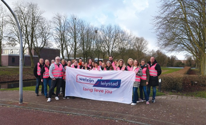 Mannen en vrouwen in roze hesjes houden vlag met logo Welzijn Lelystad vast.
