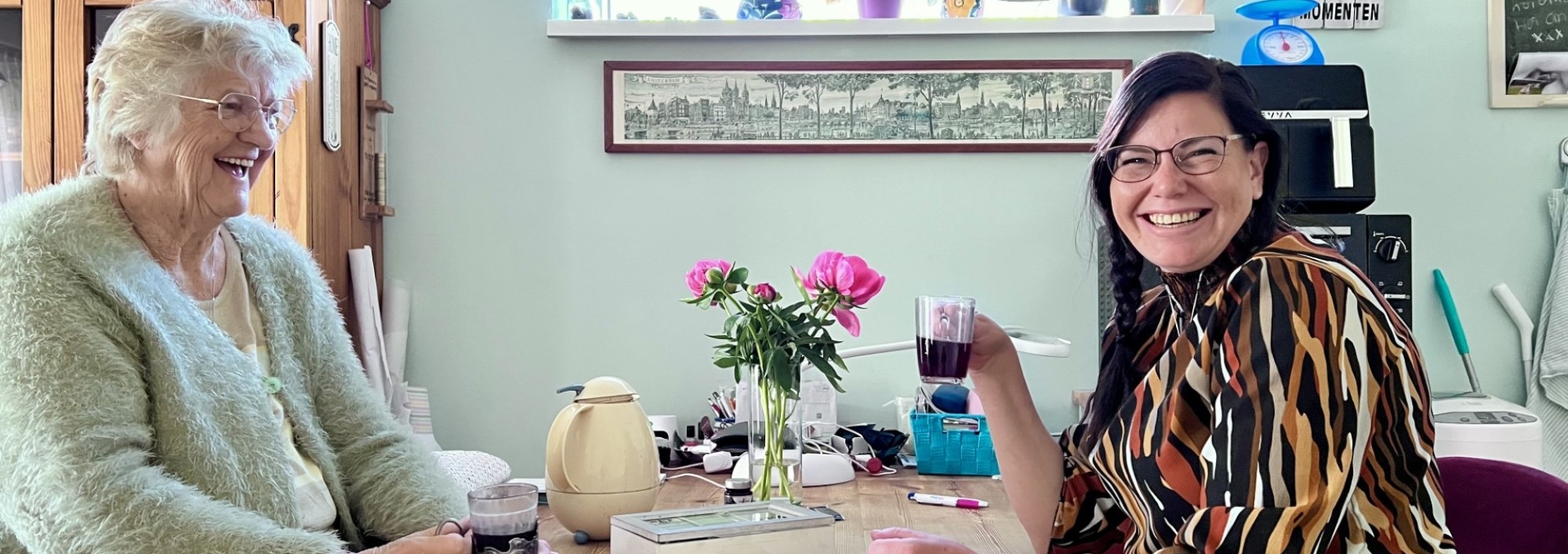 Oudere en jongere vrouwen drinken thee aan de keukentafel.