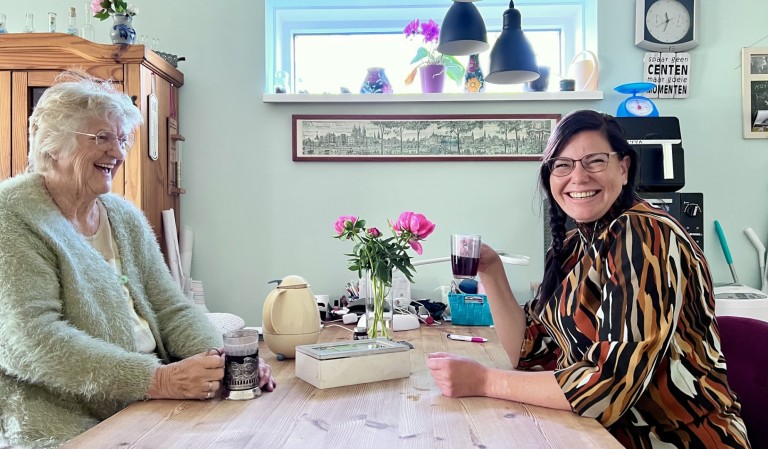 Oudere en jongere vrouwen drinken thee aan de keukentafel.