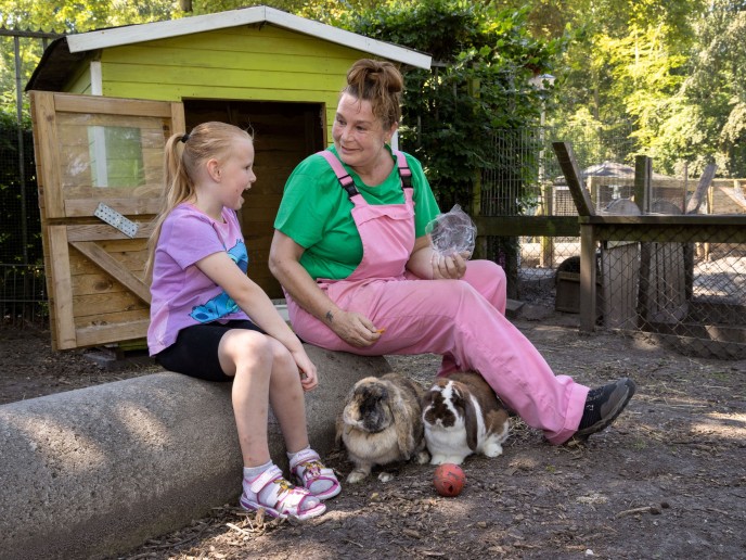 Vrouw en kind zitten op boomstam en hebben konijnen vast.