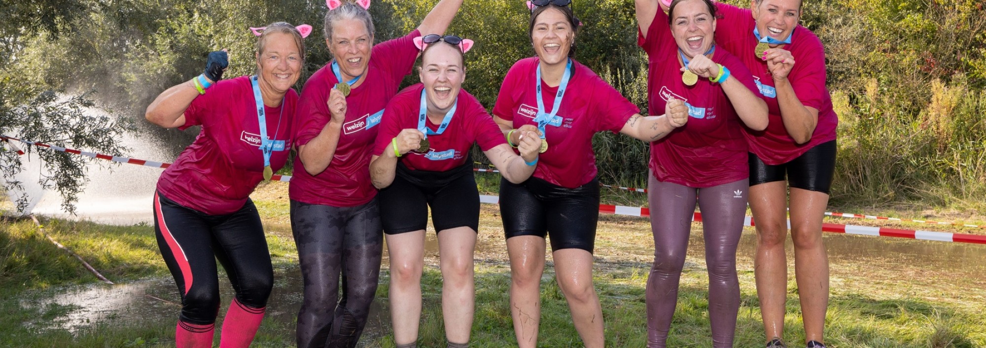 Groep vrouwen in roze shirts poseren in de modder.