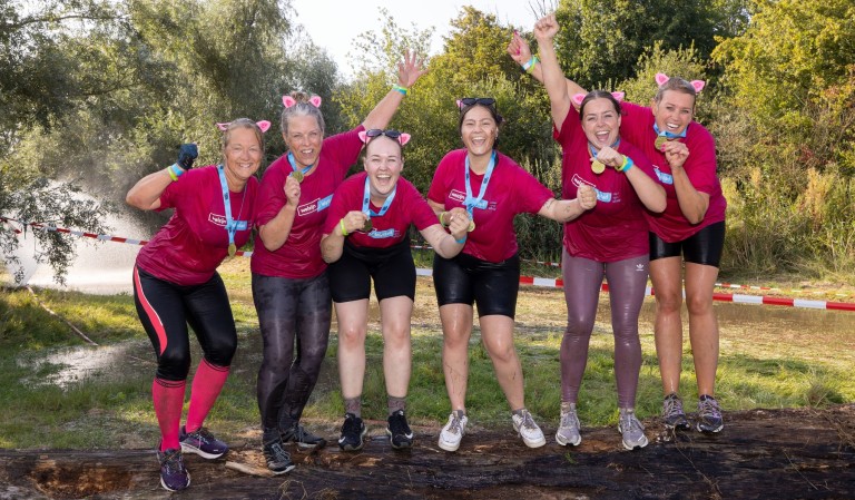 Groep vrouwen in roze shirts poseren in de modder.