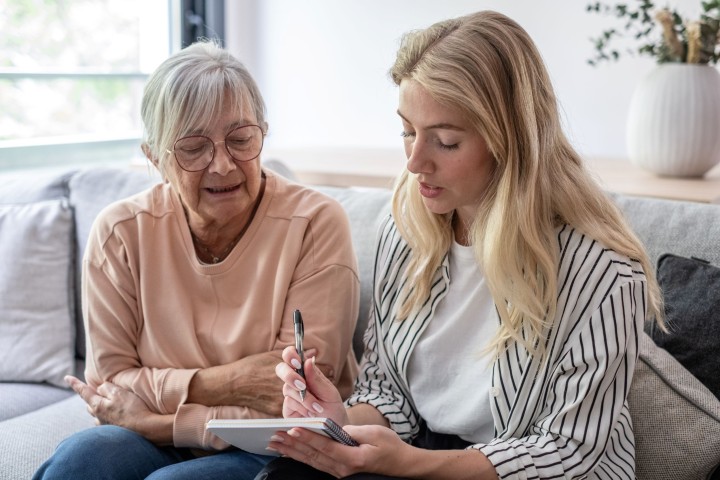 Jongere vrouw helpt oudere vrouw met invullen papieren.